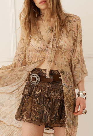 a-woman-wearing-a-bohemian-style-outfit-featuring-a-sheer-beige-paisley-cardigan-a-brown-patterned-ruffled-mini-skirt-and-a-wide-brown-belt-with-a-silver-buckle