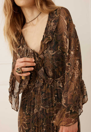 a-close-up-of-a-woman-wearing-a-brown-and-black-paisley-patterned-sheer-long-sleeve-dress-with-a-ruffled-v-neckline-and-gathered-waist