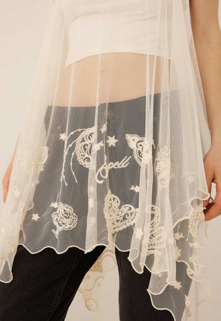 a-close-up-of-a-person-wearing-a-sheer-white-lace-overlay-draped-over-dark-gray-jeans-with-a-white-crop-top-partially-visible-the-lace-features-embroidered-celestial-motifs-including-stars-hearts-and-the-word-spell-in-script