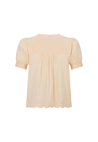 a-light-peach-colored-blouse-with-short-puff-sleeves-a-gathered-smocked-bodice-and-a-scalloped-hem-shown-against-a-plain-white-background