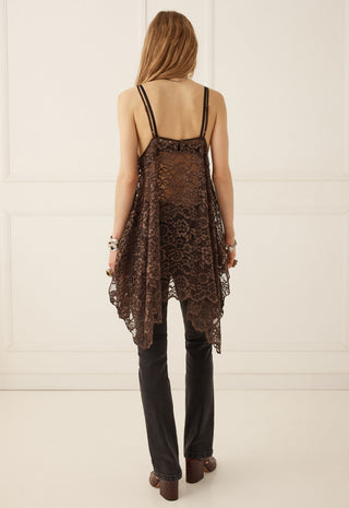 a-woman-shown-from-the-back-wearing-a-dark-brown-lace-camisole-top-with-thin-straps-black-pants-and-brown-shoes-standing-against-a-white-paneled-wall